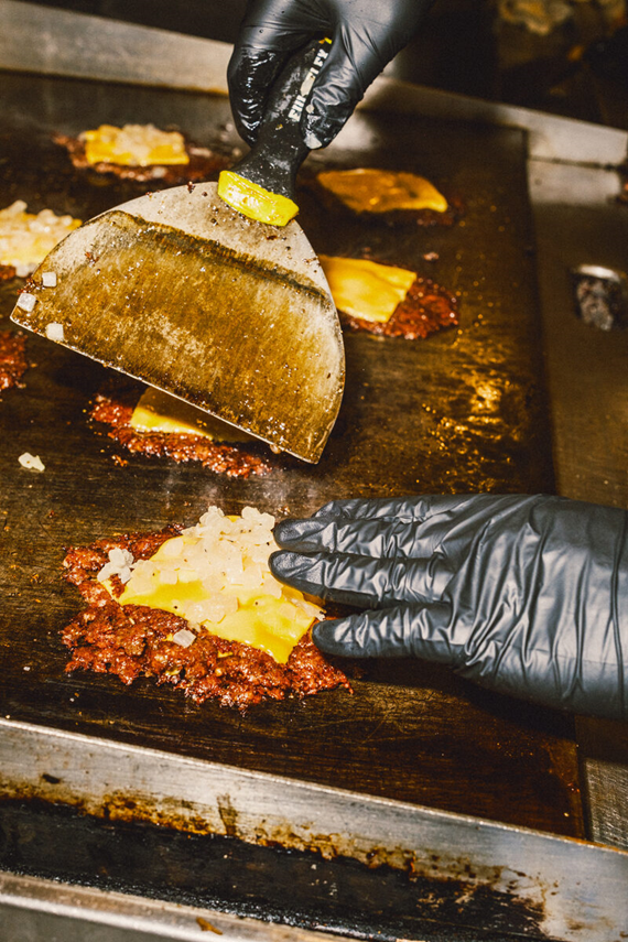 Burger Bodega cook pressing fresh beef onto a hot flat-top for a smash burger