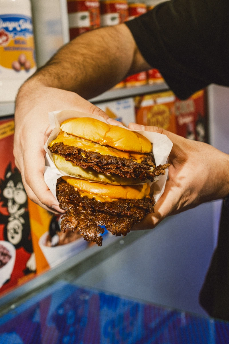 Burger Bodega double cheeseburger with two crispy beef patties and melted cheese held in hands.