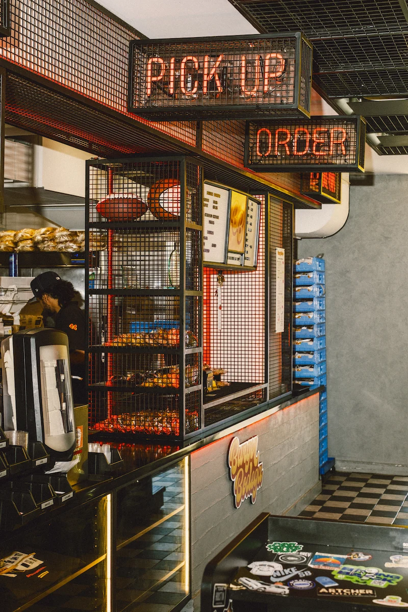 Burger Bodega restaurant counter with illuminated pickup and order signs, menu board, and branded interior.