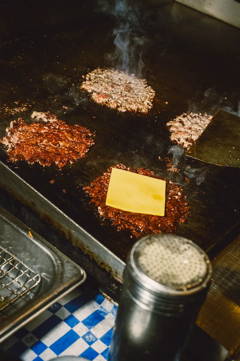 Fresh burger cooking on the Burger Bodega flat-top grill in Houston